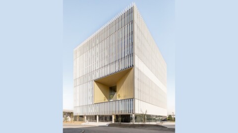 Modern geometric building with a prominent angular facade and vertical slats, set against a clear sky.