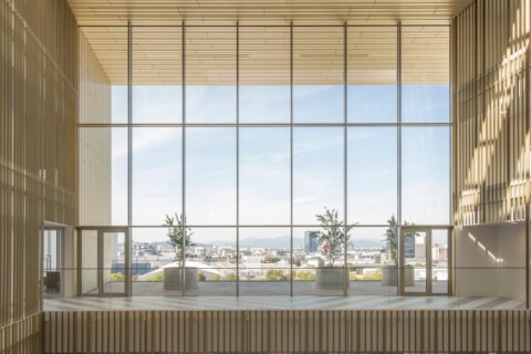 Innenraum mit grossen Fenstern, Holzverkleidung und Blick auf eine städtische Landschaft.