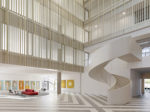 A modern interior of a spacious lobby featuring a spiral staircase, gray flooring, and a red sofa surrounded by artwork.