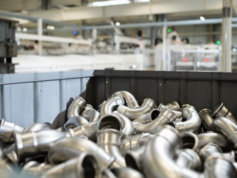 A container filled with shiny metal pipe fittings in an industrial setting.