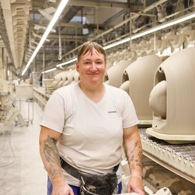 A smiling worker standing in a manufacturing facility with machinery and products in the background.