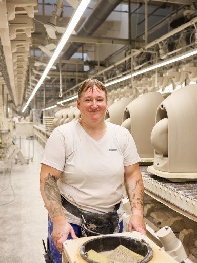 A smiling worker standing in a manufacturing facility with machinery and products in the background.