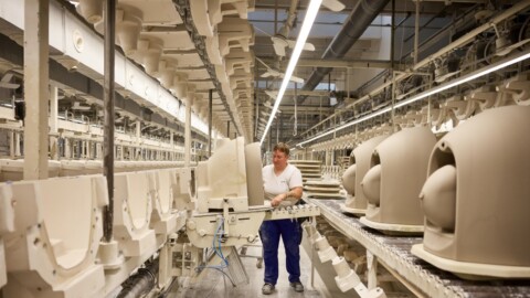 A worker operating machinery in a manufacturing facility with rows of large, beige ceramic products.
