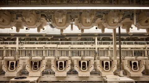 A production facility with multiple beige toilet bowls arranged in rows on assembly lines.