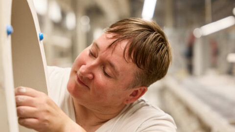 A person with short hair is working on a ceramic in a well-lit industrial setting, focused on details.