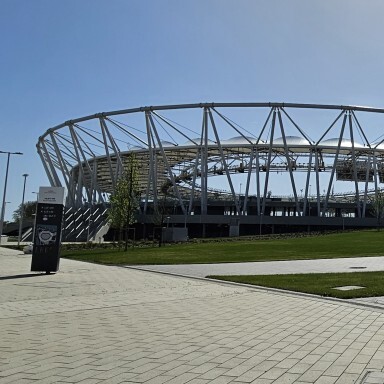 Ein modernes Stadion mit einer geschwungenen Metallkonstruktion und einem klaren blauen Himmel im Hintergrund.