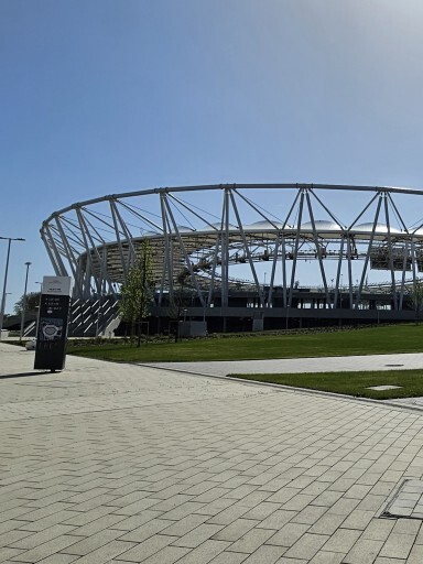 Ein modernes Stadion mit einer geschwungenen Metallkonstruktion und einem klaren blauen Himmel im Hintergrund.