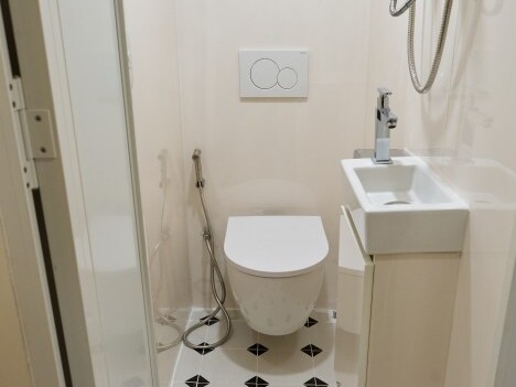 Ein modernes Badezimmer mit einem WC, einer kleinen Waschbecken und einer Dusche, sowie einem schlichten Fliesenboden.