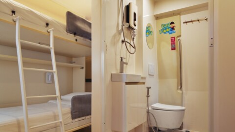 Ein Schlafzimmer mit einem Hochbett, einem kleinen Badezimmer und einer Toilette, ausgestattet mit einem Waschbecken und Handtuchhaltern.