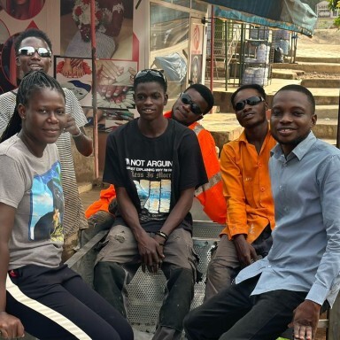A group of young people sitting together outdoors, smiling, with a mix of casual clothing.