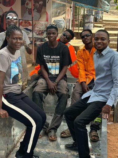 A group of young people sitting together outdoors, smiling, with a mix of casual clothing.