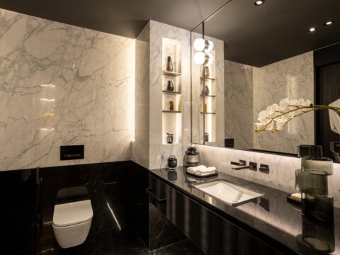 Elegantes Badezimmer mit marmorierten Wänden, einem schwarzen Waschtisch und modernen Beleuchtungselementen.
