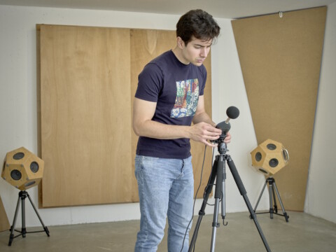 Ein junger Mann stellt ein Mikrofon auf einem Stativ in einem Raum mit akustischen Schalldämpfern und Lautsprechern ein.