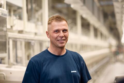Ein lächelnder Mann steht in einer modernen, hellen Produktionsumgebung.