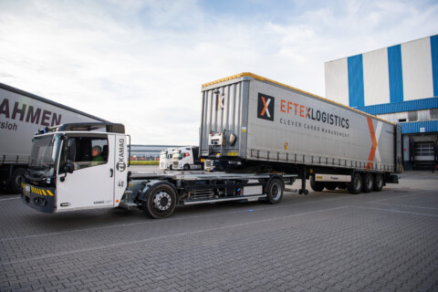 Ein Lkw mit einem Auflieger steht auf einem gepflasterten Parkplatz vor einem Lagergebäude.