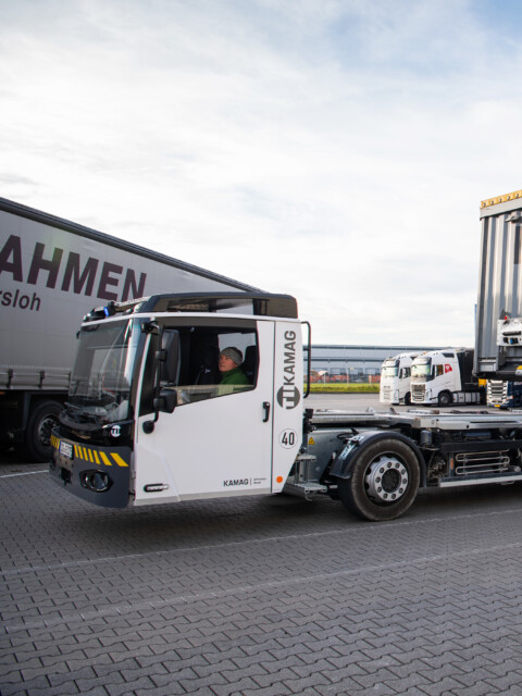 A lorry parked next to a loading dock, with a blue and white warehouse in the background.