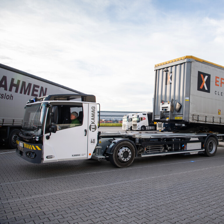 A lorry parked next to a loading dock, with a blue and white warehouse in the background.