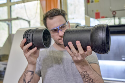 Ein Mann mit Schutzbrille hält zwei schwarze Kunststoffrohre in beiden Händen und betrachtet sie aufmerksam.