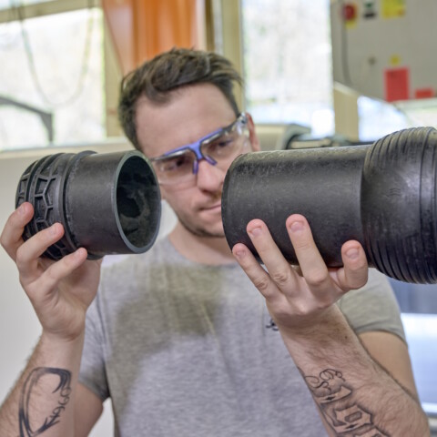 A person wearing protective glasses examines two black plastic pipes.