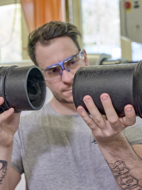 A person wearing protective glasses examines two black plastic pipes.