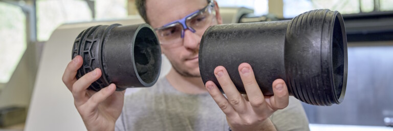 A person wearing protective glasses examines two black plastic pipes.
