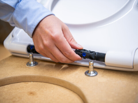 A person is attaching a device using a black connector to a white object on a wooden surface.