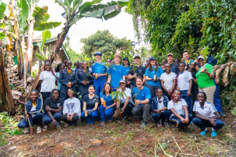 Eine grosse Gruppe von Menschen steht in einer natürlichen Umgebung, umgeben von Pflanzen und Bäumen, während sie lächeln und posieren.