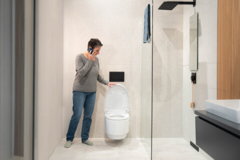 Eine Person spricht am Telefon, während sie neben einer modernen Toilette in einem Badezimmer steht.