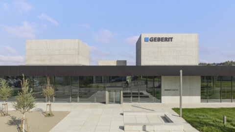 Moderne Unternehmensarchitektur mit betonsichtbaren Würfeln und Glasfassade, begrüntem Areal und gepflastertem Eingang.