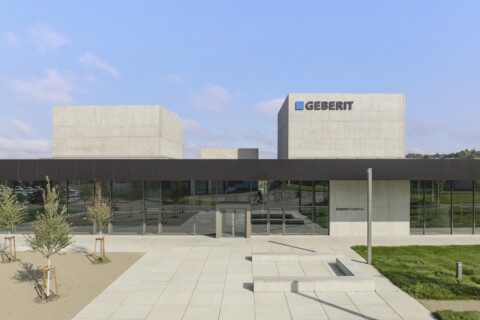Modern building with a geometric design featuring large glass windows, surrounded by landscaped green areas.