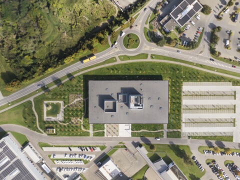 An aerial view of a modern building surrounded by greenery, parking lots, and circular roads.