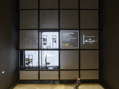 A modern exhibition wall divided into large grid sections, with installations and a person standing in front.