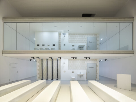 Modern interior space featuring transparent glass walls, minimalistic design, and white benches arranged in rows.