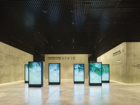 A modern exhibition space featuring several tall digital screens displaying nature.