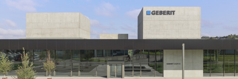 Modern building with a geometric design featuring large glass windows, surrounded by landscaped green areas.