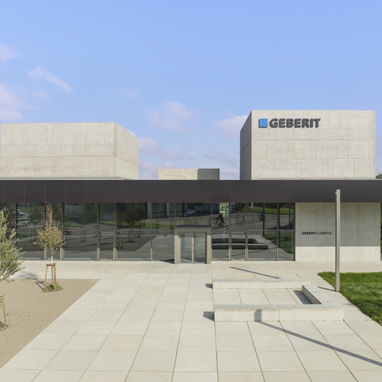 Modern building with a geometric design featuring large glass windows, surrounded by landscaped green areas.