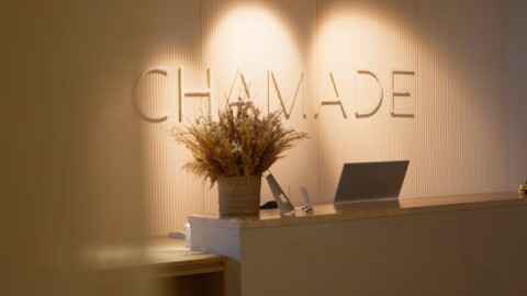 Empfangstheke mit beleuchtetem Schriftzug "CHAMADE" und dekorativem Pflanzenschmuck.