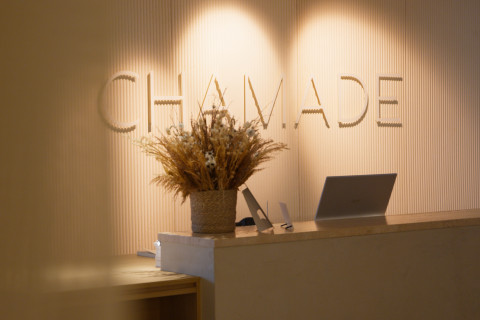 Empfangstheke mit beleuchtetem Schriftzug "CHAMADE" und dekorativem Pflanzenschmuck.