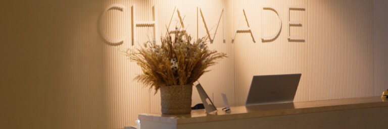 Reception area with the word "CHAMADE" on the wall and a decorative plant arrangement on a counter.