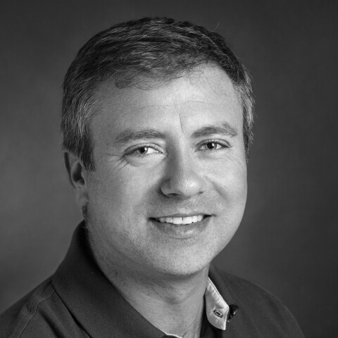 Porträt eines lächelnden Mannes mit kurzen Haaren. Ein schwarz-weiss Bild.