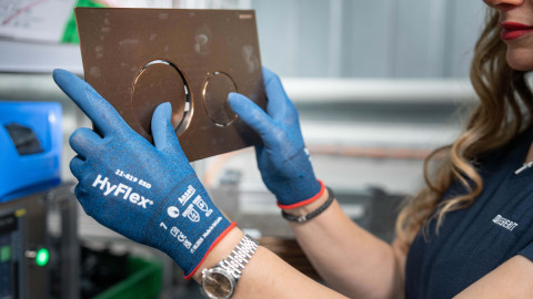 A person wearing blue gloves examines an actuator plate with round buttons.