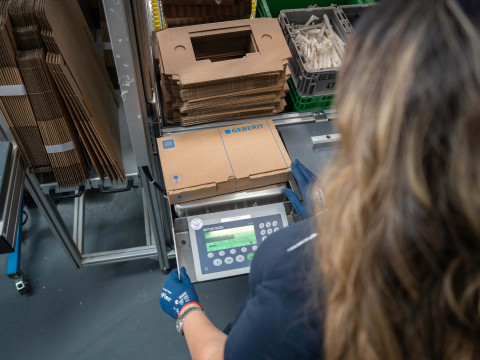 A person using a digital scale to weigh cardboard boxes in a warehouse setting.