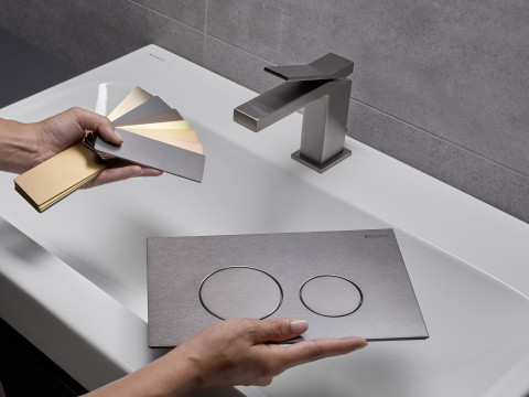 A person holding colour samples and a actuator plate over a modern sink with a sleek faucet.