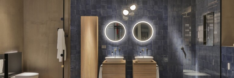 Moderne Badezimmeransicht mit blauen Fliesen, zwei Waschbecken, runden Spiegeln und einer separaten Duschkabine.