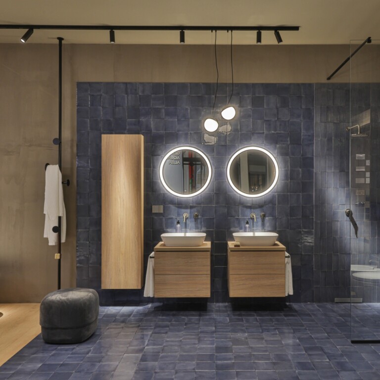 Moderne Badezimmeransicht mit blauen Fliesen, zwei Waschbecken, runden Spiegeln und einer separaten Duschkabine.