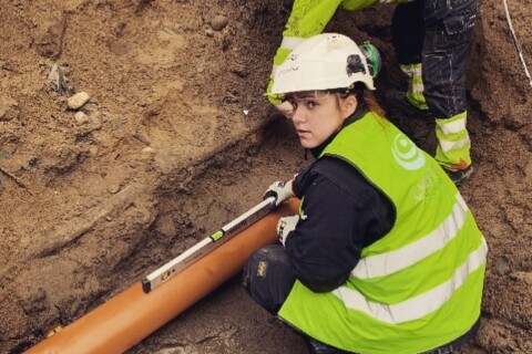 Two workers in safety gear are installing a large pipe in a trench.