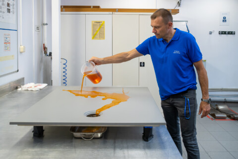 A man in a blue shirt pours a fluid from a measuring jug onto the Geberit CleanFloor30.