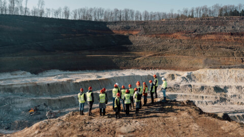 A group of people wearing safety vests stands at the edge of Trench.