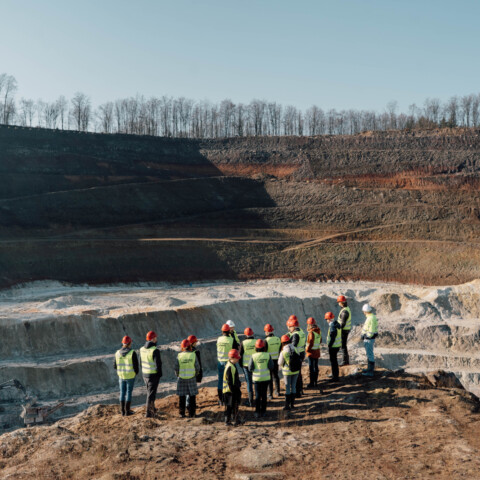Eine Gruppe von Personen in Warnwesten steht an einer Tongrube mit sichtbaren Erdschichten.