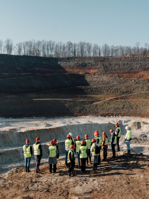 A group of people wearing safety vests stands at the edge of Trench.